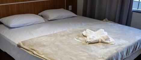 Una cama bien tendida con edredón blanco y manta color beige, un cabecero de madera y un teléfono junto a la cama.