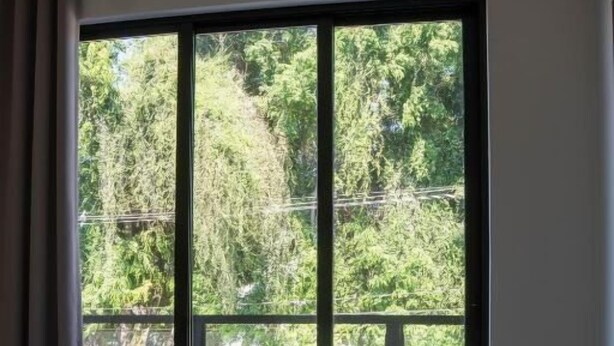 Ein Hotelzimmer mit großem Fenster, einem Bett und Blick auf Bäume sowie parkende Autos vor dem Haus.
