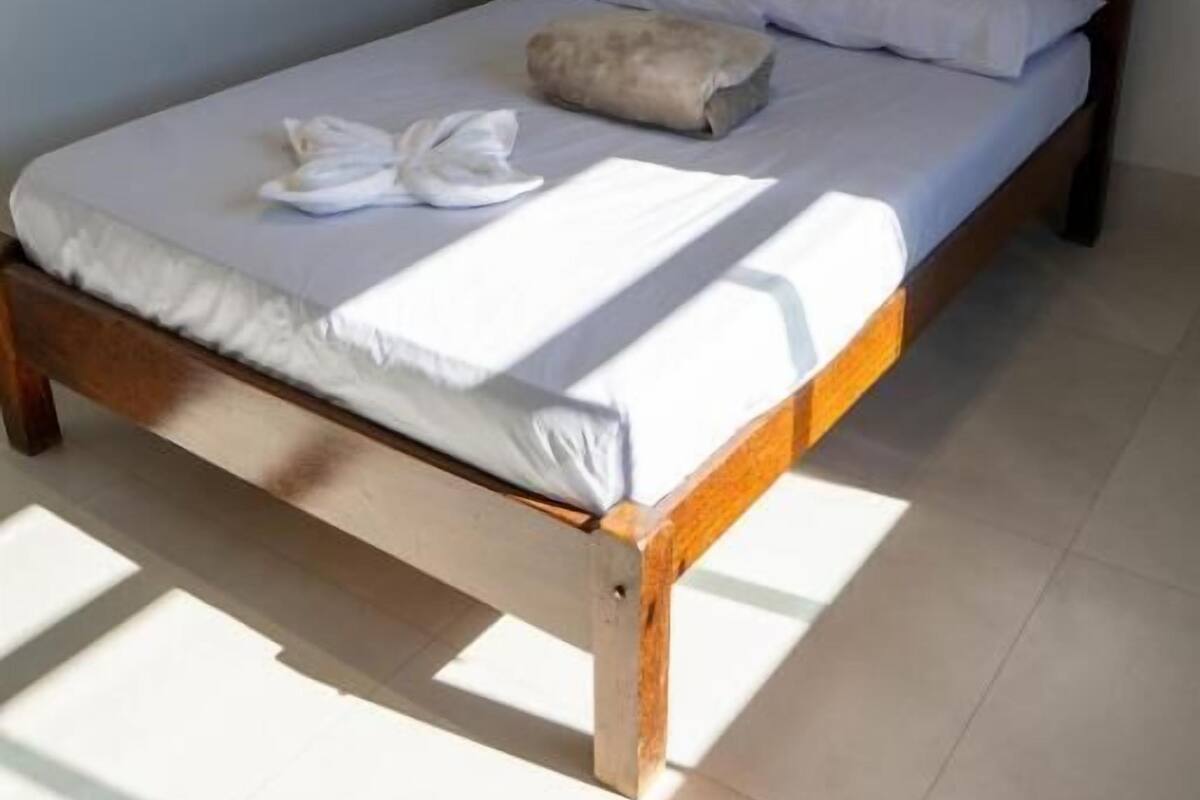 Een enkel bed met houten frame, wit beddengoed en een kussen.