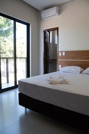 Una habitación de hotel con una cama, un ventanal grande y un equipo de aire acondicionado.