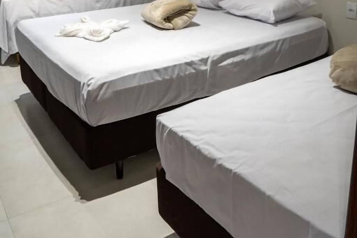 Een hotelkamer met twee enkele bedden, een raam met gordijnen, een airconditioning en een betegelde vloer.