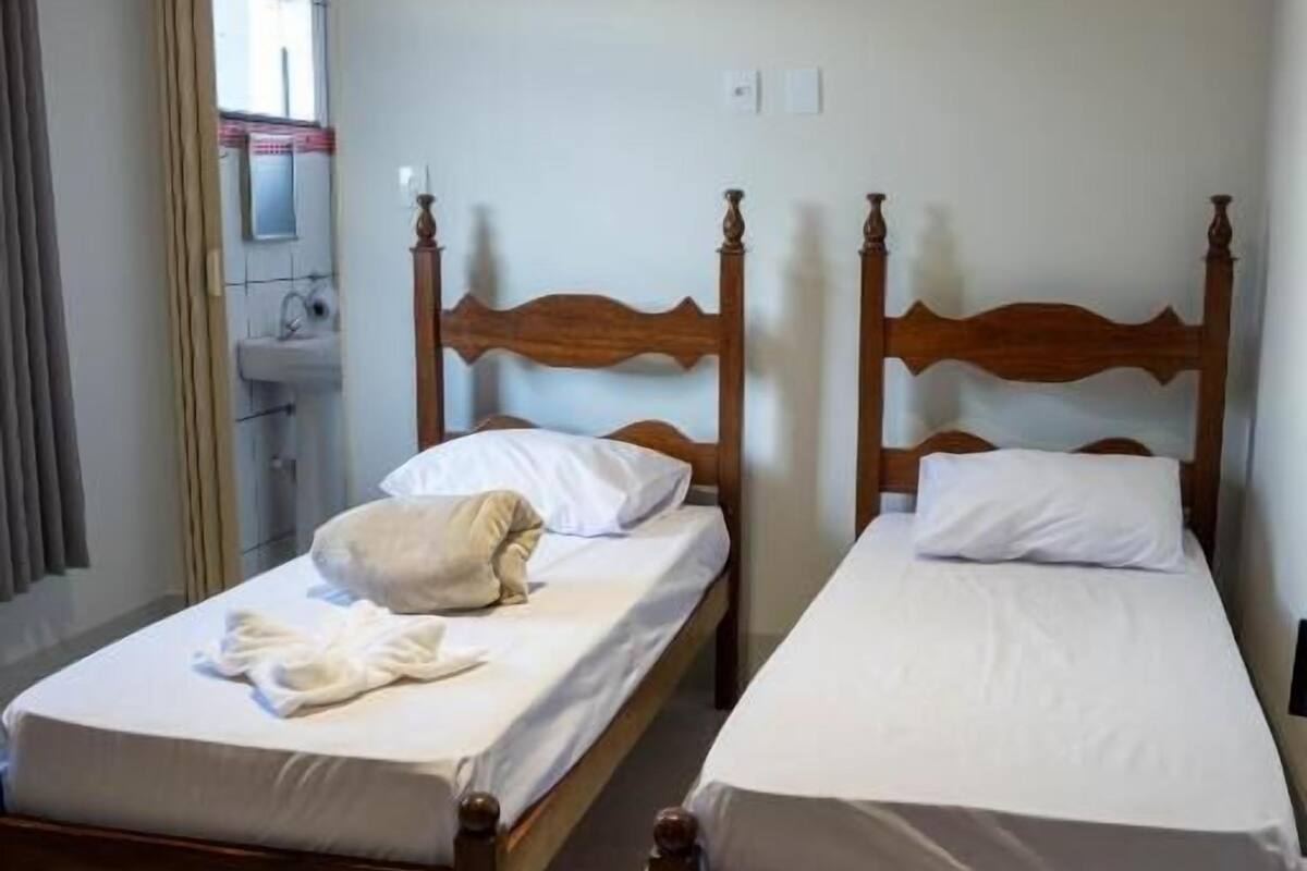 Een tweepersoonskamer met twee houten bedden, een badkamer met een wastafel en een spiegel.