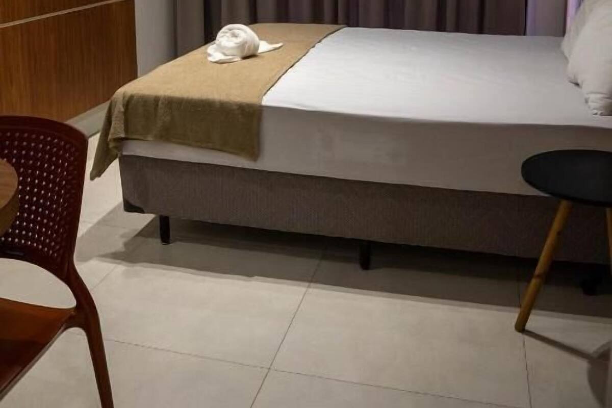 Een hotelkamer met een bed, een aan de muur bevestigde televisie, een raam met gordijnen en een stoel.