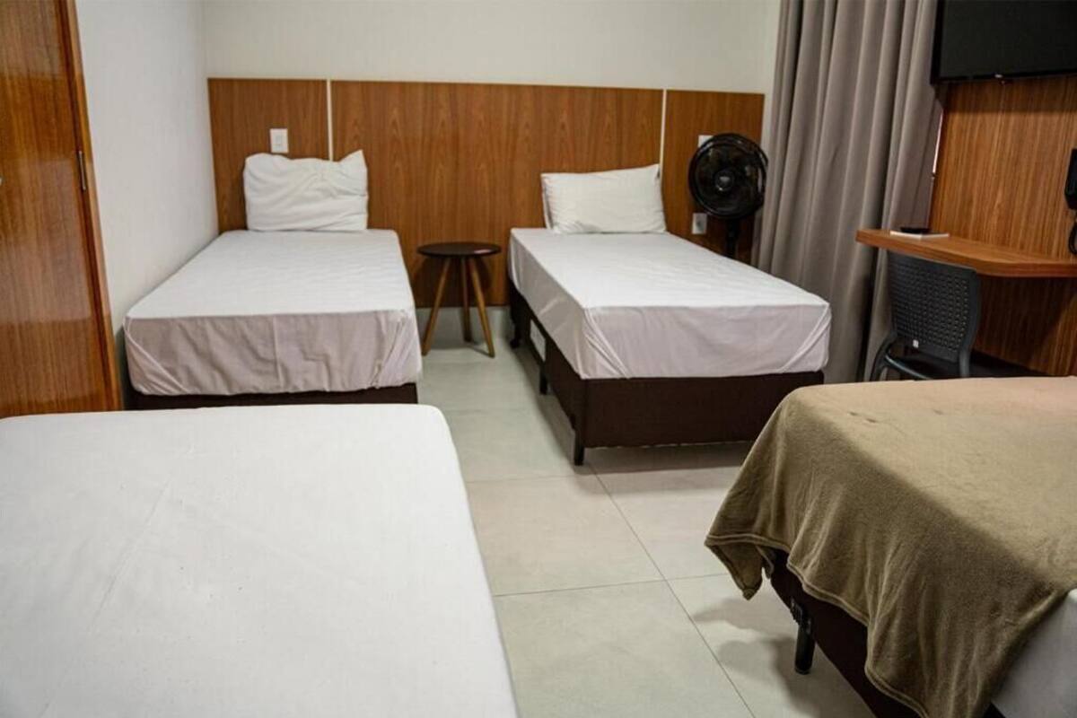 Een hotelkamer met twee eenpersoonsbedden, een houten hoofdbord, een klein tafeltje, een ventilator en een televisie.