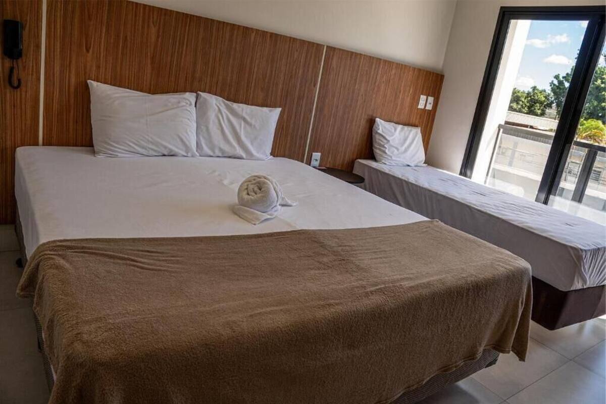 Een hotelkamer met een groot bed, een kleiner bed, een houten hoofdeinde en uitzicht door een raam.