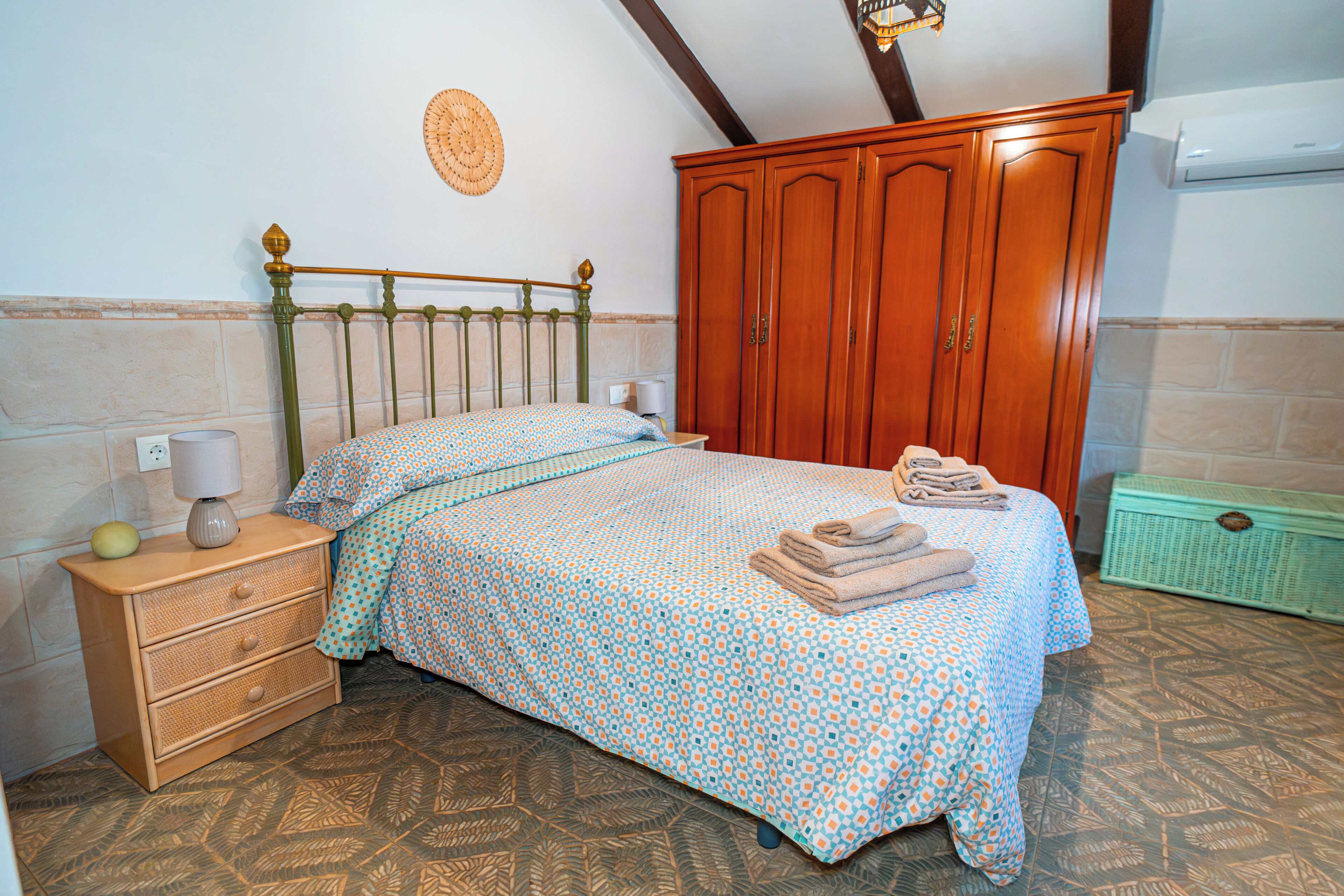 Une chambre à coucher comprenant un lit, une armoire en bois, une table de chevet, une lampe et un radiateur fixé au mur.