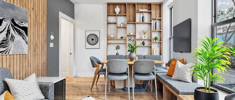 Un salon moderne comprenant un coin repas, des murs recouverts de panneaux en bois, un téléviseur à écran plat et une grande fenêtre.