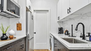 A narrow kitchen with white cabinets, a stainless steel refrigerator, a dishwasher, and a sink with a black faucet. - Two Bedroom - Newly Renovated - Washer/Dryer in New York City (New York)