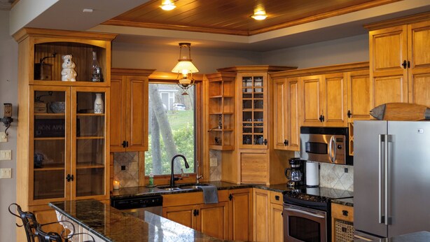 Una cocina con armarios de madera, encimera de granito, refrigerador de acero inoxidable y una zona de bar con taburetes.