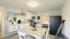 Een kleine keuken met witte kastjes, een magnetron, een koffiezetapparaat, en een eethoek met een tafel en stoelen.
