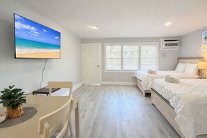 A bedroom with two beds, a TV on the wall, a window with blinds, and a small table with a plant. - Sun-Joy Getaway #5 | Near Boardwalk, Walk to Beach (Myrtle Beach)