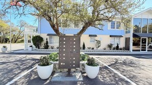 Un edificio con techo azul, un árbol grande en primer plano y un cuadro de electricidad con varios compartimentos.