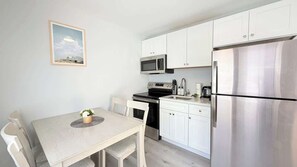 A modern kitchen with white cabinets, a stainless steel refrigerator, a microwave, and an oven. There is a dining table with chairs and a small plant on the table. - Sun-Joy Stay #10 | 5-Min Walk to Beach (Myrtle Beach)