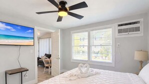 Una camera da letto con un letto, un ventilatore a soffitto, una TV e una finestra con persiane.