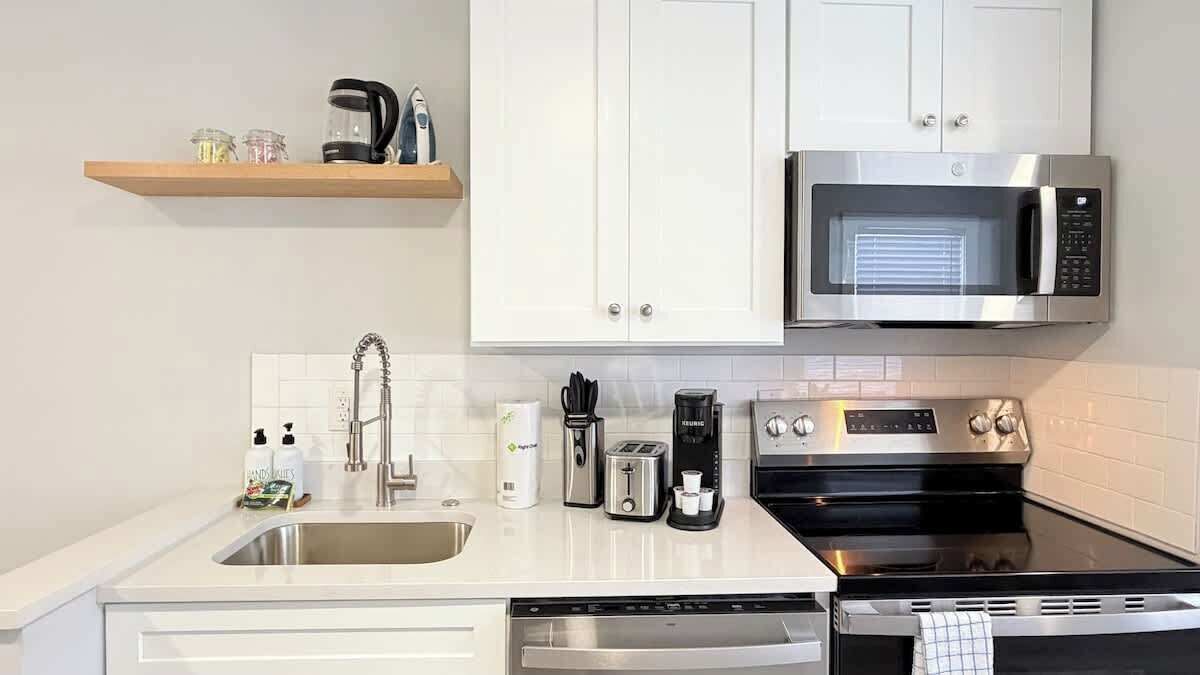 A modern kitchen with white cabinets, a stainless steel microwave, a coffee maker, a toaster, and a dishwasher.
