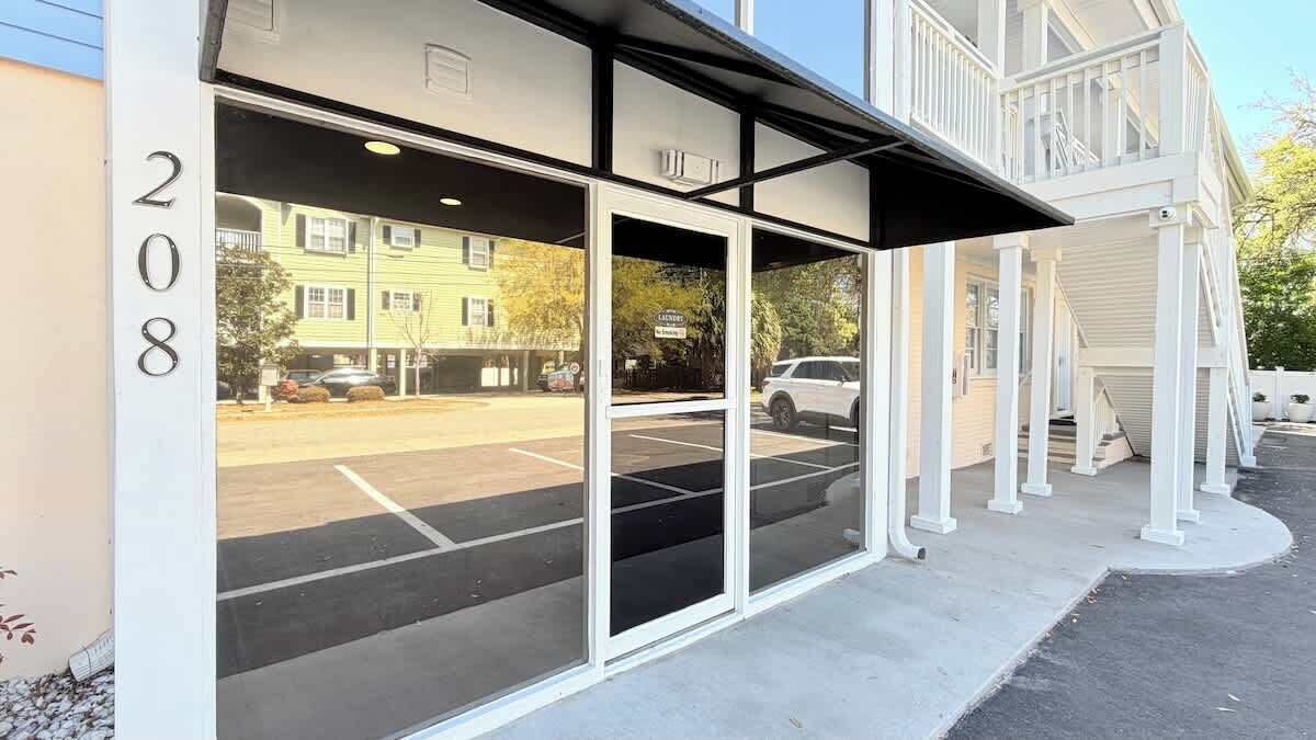 A building with a glass entrance, a visible address number, and a parking lot.
