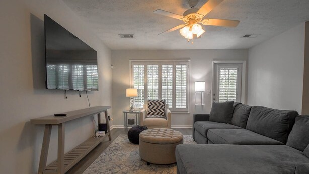 A living room with a flat-screen TV, a ceiling fan, a sofa, an ottoman, and a chair. - Saturdays on Donahue (Auburn)