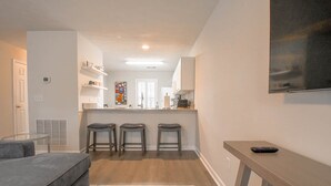 A modern kitchen with a central island, bar stools, a grey sofa, and a TV mounted on the wall. - Saturdays on Donahue (Auburn)