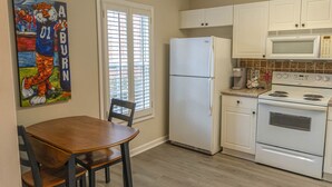 A kitchen with white cabinets, a refrigerator, a microwave, and a stove. There is a dining table with chairs and a window with blinds. - Saturdays on Donahue (Auburn)