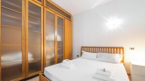 Ein Hotelzimmer mit einem Bett, weißen Leinentextilien, einem Holzkopfende, einem Schrank mit Milchglas-Türen und einer Wandleuchte.