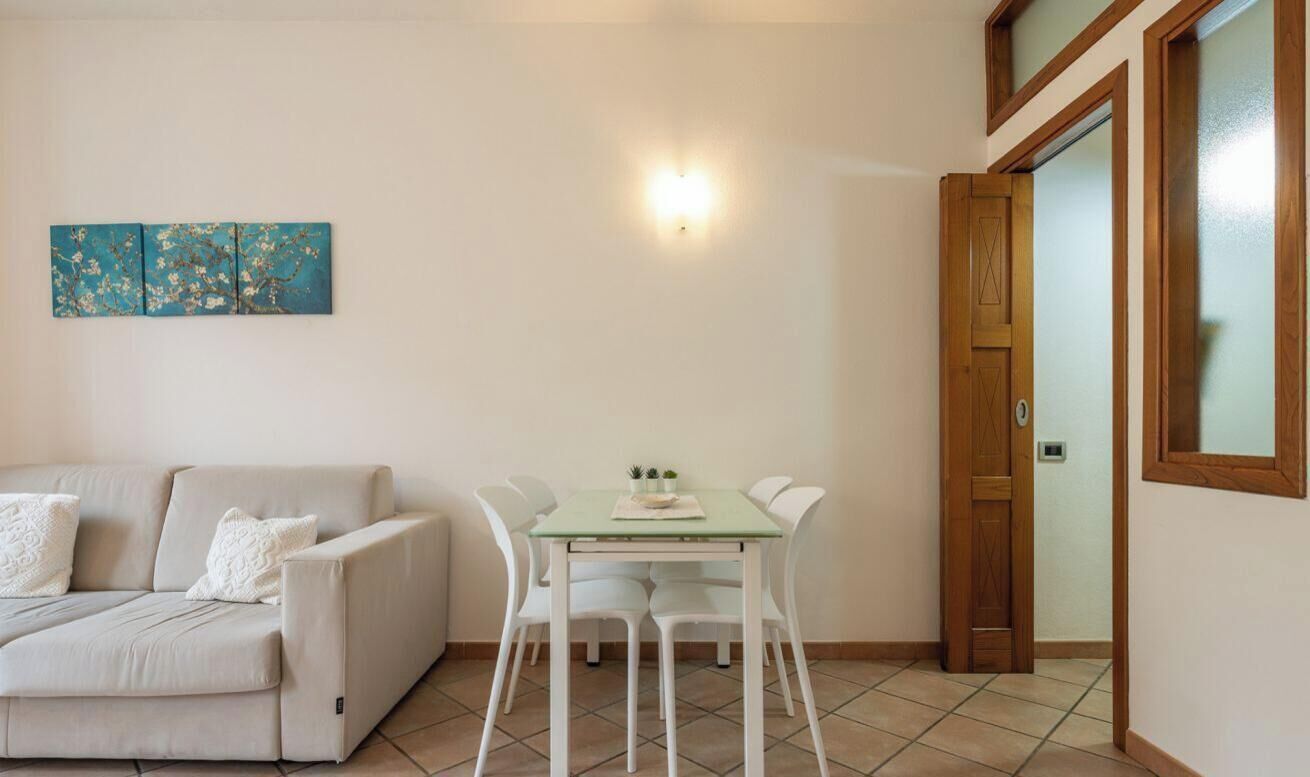 Un salon comprenant un canapé, une table à manger avec des chaises, un luminaire fixé au mur et une porte.