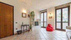 Ein Wohnzimmer mit Holztür, Fliesenboden, einem roten Sitzsack, einem Fernseher, einer Pflanze und einem Balkon mit Blick.