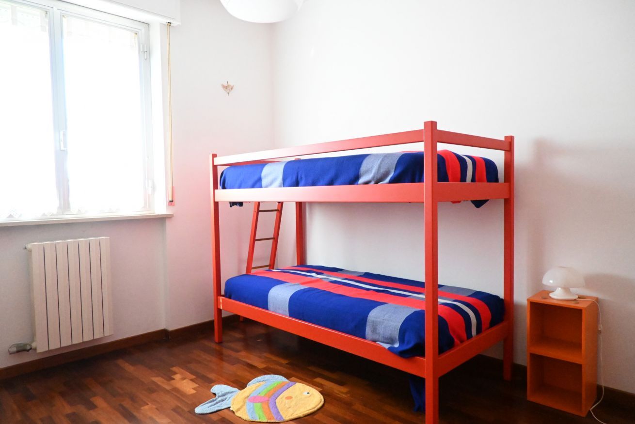 A bunk bed with a ladder, a small shelf, a radiator, and a window.