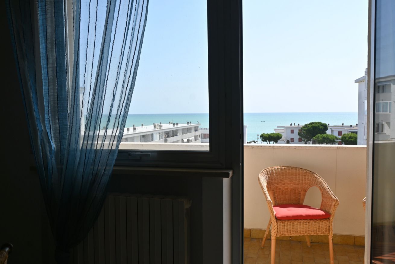 A balcony with a wicker chair and a view of the sea and buildings.