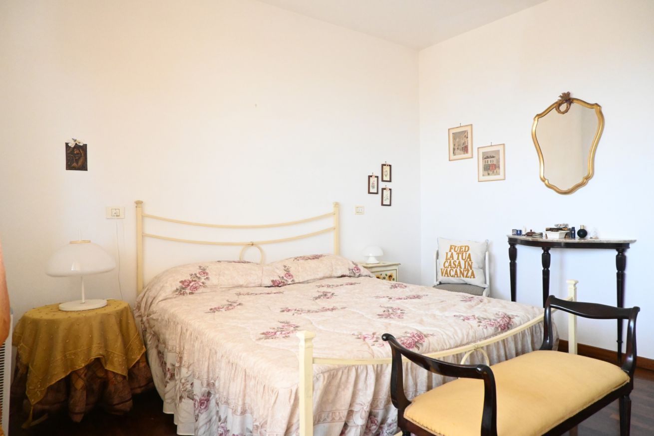 A bedroom with a bed, bedside table, lamp, chair, and a mirror on the wall.
