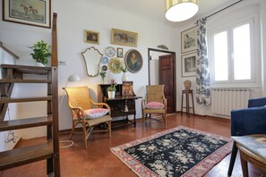 Una habitación con escalera de madera, sillas de mimbre, alfombra estampada y varias fotografías enmarcadas en las paredes.