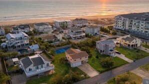 A residential area with houses, a swimming pool, and a view of the ocean at sunset. - New! Beach Cottage, Pool, PickleBall, Swim, Surf (Virginia Beach)