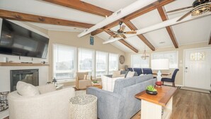 A modern living room with a fireplace, a television, and a dining area with a wooden table. - New! Beach Cottage, Pool, PickleBall, Swim, Surf (Virginia Beach)