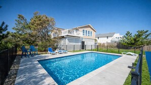 A rectangular swimming pool with a wooden deck, surrounded by a black fence. - New! Beach Cottage, Pool, PickleBall, Swim, Surf (Virginia Beach)