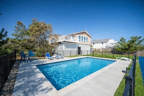 A rectangular swimming pool with a wooden deck, surrounded by a black fence. - New! Beach Cottage, Pool, PickleBall, Swim, Surf (Virginia Beach)