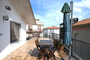 A patio with a table and chairs, a green umbrella, and a white building with a balcony.