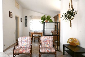 A room with two floral-patterned chairs, a wooden table, a hanging plant, and a decorative fan.