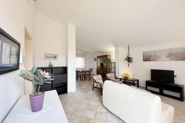 A living room with a sofa, TV stand, and a dining area with chairs and a table.