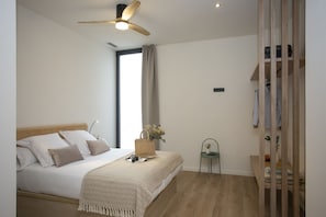 Ein Schlafzimmer mit einem Bett, einem Deckenventilator, einem Fenster mit Vorhängen, einem Sessel und einem Holzschrank.