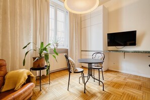 Una sala de estar con sofá, una mesa de comedor con sillas, un televisor montado en la pared y una planta en maceta.