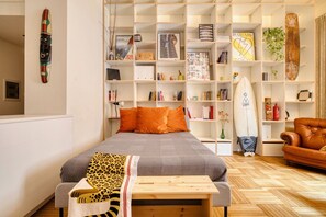 Un dormitorio con una cama, una mesita de noche de madera, una estantería y una tabla de surf.