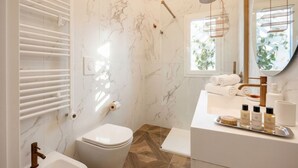 A bathroom with a marble wall, a shower with a glass door, a toilet, a sink with toiletries, and a window with natural light. - Sfazion - Central Apartment (Bari)