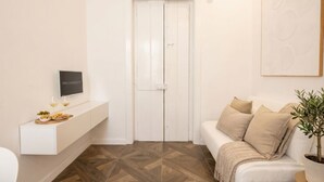 A modern room with a white door, a mounted TV, a white sofa, and a potted plant. - Sfazion - Central Apartment (Bari)