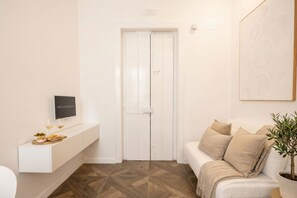 Una camera moderna con una porta bianca, una TV a parete, un divano bianco e una pianta in vaso.