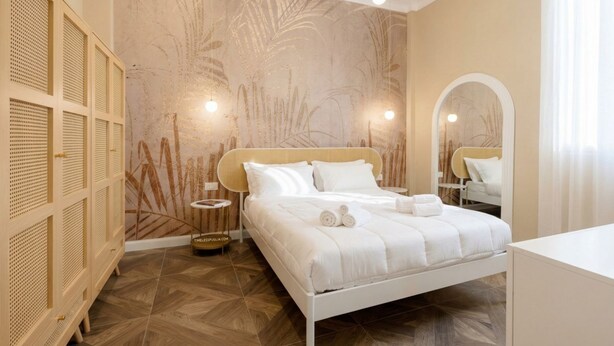 A bedroom with a bed, a wardrobe, a mirror, and a wall with a leaf pattern. - Sfazion - Central Apartment (Bari)