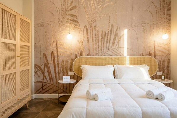 Ein Zimmer mit einem Bett, einem runden Kopfteil, einer Wand mit Blattmuster, einem kleinen Tisch und einer Lampe.
