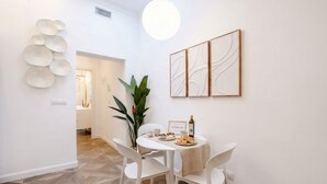 A dining area with a round table, white chairs, a potted plant, and wall art. - Sfazion - Central Apartment (Bari)