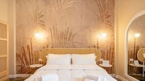 A hotel room with a large bed, two bedside tables, a wall with a plant mural, and a mirror. - Sfazion - Central Apartment (Bari)