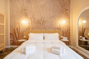 Una camera d'albergo con un letto grande, due comodini, un muro con un affresco vegetale e uno specchio.
