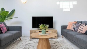 A modern living room with two grey sofas, a wooden coffee table with a plant, a TV on a wooden stand, and a large green plant.