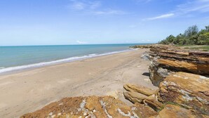 A beach with clear skies, a sandy shore, and rocky outcrops.
